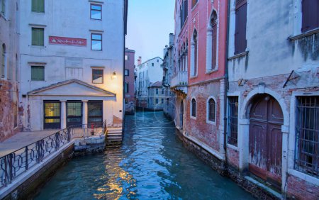 Photo for VENICE, ITALY - APRIL 10 2023: A narrow Venetian canal illuminated by twilights soft glow, flanked by ancient buildings including the historical home of Marco Polo. - Royalty Free Image