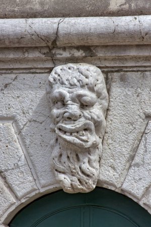 Téléchargez les photos : VENISE, ITALIE - 11 AVRIL 2023 : Un vieux relief du masque grotesque comme élément décoratif sur une façade de vieilles maisons au-dessus de la porte d'entrée. - en image libre de droit