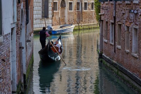 Foto de VENECIA, ITALIA - 11 ABRIL 2023: Un gondolero navega hábilmente por un sinuoso canal en el centro histórico de Venices, ofreciendo un vistazo al encanto atemporal de esta icónica ciudad. - Imagen libre de derechos