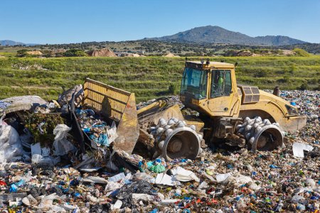 Heavy machinery shredding garbage in an open air landfill. Waste