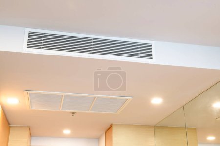 Kanalklimaanlage für zu Hause oder im Büro. Deckenmontierte Klimaanlage vom Typ Kassette und modernes Lampenlicht an der weißen Decke.