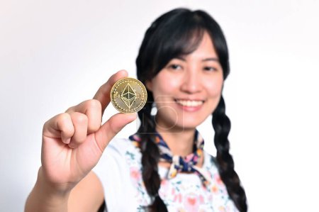Foto de Portrait beautiful happy young asian woman in denim dress holding crypto currency coin on white background. - Imagen libre de derechos