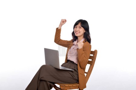 Photo for Happy young business asian woman celebrating on her success. While her using laptop sitting on wooden chair isolate on white background - Royalty Free Image
