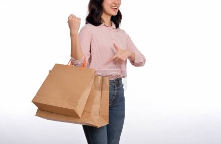 Téléchargez les photos : Jeune femme asiatique heureuse avec chemise décontractée et jeans en denim tenant sac de papier shopping isolé sur fond blanc. - en image libre de droit