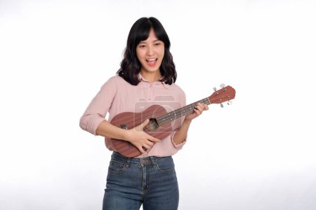 Foto de Feliz joven asiático mujer con casual ropa jugando ukelele aislado en blanco fondo - Imagen libre de derechos