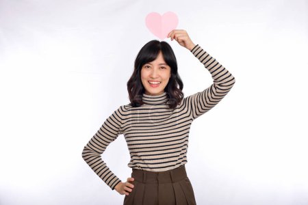 Téléchargez les photos : Belle jeune femme asiatique avec coeur en papier. Belle jeune femme asiatique tenant un cœur en papier tout en se tenant sur fond blanc - en image libre de droit