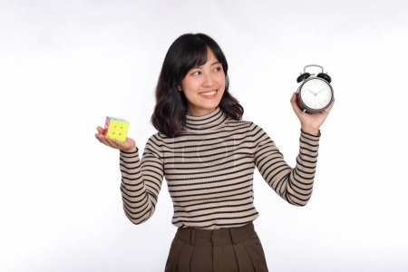 Téléchargez les photos : Femme asiatique tenant réveil et puzzle cube debout sur fond blanc. résoudre des problèmes cubiques, solution de problème et faire des mouvements stratégiques concept. - en image libre de droit
