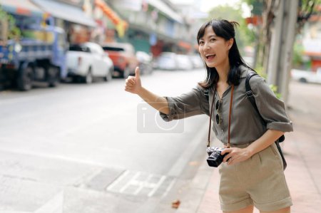 Foto de Sonriente joven mujer asiática viajero autoestop en un camino en la ciudad. - Imagen libre de derechos