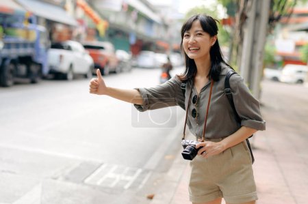 Téléchargez les photos : Smiling young Asian woman traveler hitchhiking on a road in the city. - en image libre de droit