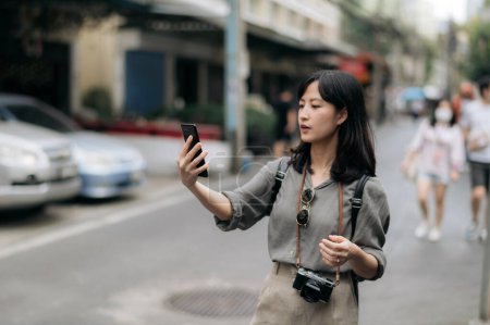 Foto de Young Asian woman backpack traveler using mobile phone, enjoying street cultural local place. - Imagen libre de derechos