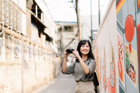 Photo for Young Asian woman backpack traveler using digital compact camera, enjoying street cultural local place and smile. - Royalty Free Image