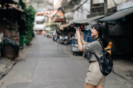 Photo for Young Asian woman backpack traveler using digital compact camera, enjoying street cultural local place and smile. - Royalty Free Image