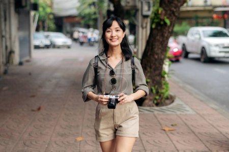 Photo for Young Asian woman backpack traveler using digital compact camera, enjoying street cultural local place and smile. Traveler checking out side streets. - Royalty Free Image