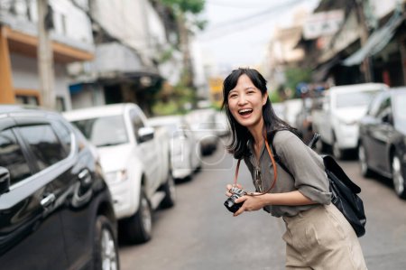 Photo for Young Asian woman backpack traveler using digital compact camera, enjoying street cultural local place and smile. Traveler checking out side streets. - Royalty Free Image