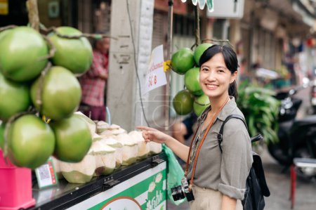 Téléchargez les photos : Happy young Asian woman backpack traveler stand in front of coconut juice shop at China town street food market in Bangkok, Thailand. - en image libre de droit