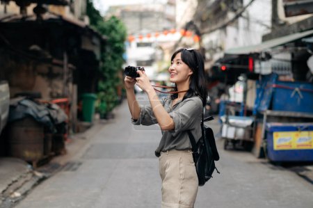 Téléchargez les photos : Young Asian woman backpack traveler using digital compact camera, enjoying street cultural local place and smile. - en image libre de droit