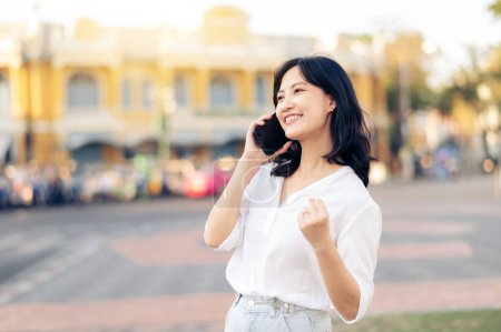 Téléchargez les photos : Portrait belle jeune femme asiatique recevant de bonnes nouvelles sur téléphone mobile autour de la vue de rue en plein air dans la journée d'été - en image libre de droit