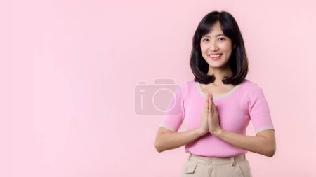 Photo for Portrait young beautiful asian woman happy smile with Sawasdee, hello gesture in Thai culture Siam traditional greeting style isolated on pink pastel background. - Royalty Free Image