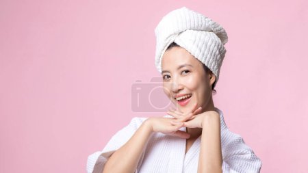 Téléchargez les photos : Jeune belle femme asiatique heureuse avec une peau de visage propre en serviette et peignoir, costume de spa sur fond rose. Soins de la peau, traitement, thérapie de bien-être, soins du visage, beauté santé féminine, concept de cosmétologie - en image libre de droit