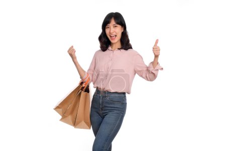 Foto de Joven mujer asiática feliz con camisa casual y vaqueros vaqueros sosteniendo bolsa de papel de compras sobre fondo blanco. - Imagen libre de derechos