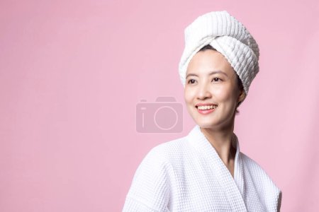 Téléchargez les photos : Belle jeune femme asiatique heureuse avec peau de visage propre en serviette et peignoir, costume de spa sur fond rose. Soins de la peau, traitement, thérapie de bien-être, soins du visage, beauté santé féminine, concept de cosmétologie - en image libre de droit