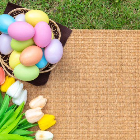Photo for Happy Easter holiday greeting card concept. Colorful Easter Eggs and spring flowers on Papyrus rattan weave texture background. Top view, flat lay, copy space. - Royalty Free Image