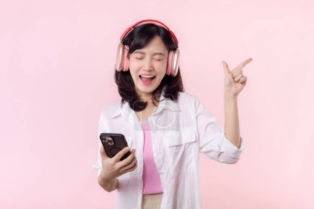 Photo for Happy smiling young asian woman close eyes and dancing relaxed with smartphone, listening music in wireless headphones. People emotions, lifestyle leisure and beauty concept. - Royalty Free Image