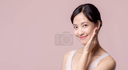 Foto de Joven hermosa mujer asiática sonrisa feliz con la piel limpia de la cara en sujetador marrón, traje de spa sobre fondo rosa. Cuidado de la piel, tratamiento, terapia de bienestar, cuidado facial, salud femenina de belleza, concepto de cosmetología - Imagen libre de derechos