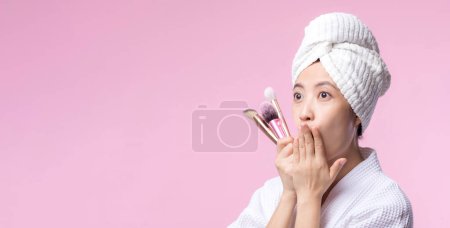 Téléchargez les photos : Portrait jeune femme asiatique heureuse avec naturel maquillage visage tenant peau cosmétique poudre rougisseur isolé sur fond rose. Femme appliquer un traitement de brosse de soins de la peau. produit de beauté, concept de cosmétologie. - en image libre de droit
