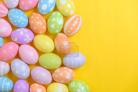 Frohe Osterfeiertage. Eine Gruppe bunt bemalter Eier auf gelbem Hintergrund. Gestaltung saisonaler Religionstradition. Draufsicht, Kopierraum, flache Lage.