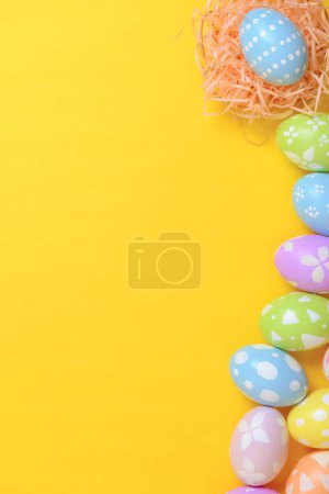 Photo for Happy easter celebration holiday. colourful pastel painted eggs in wicker basket nest decoration on a yellow background. Seasonal greeting gift card concept. Flat lay, top view, copy space. - Royalty Free Image