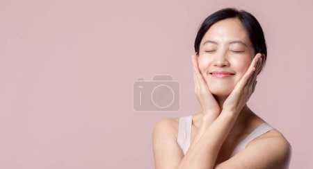 Téléchargez les photos : Jeune belle femme asiatique sourire heureux avec peau propre visage en soutien-gorge marron, costume spa sur fond rose. Soins de la peau, traitement, thérapie de bien-être, soins du visage, beauté santé féminine, concept de cosmétologie - en image libre de droit