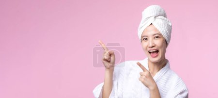 Téléchargez les photos : Jeune belle asiatique femme heureux sourire visage avec main ou doigt geste signes dans peignoir et serviette de douche montrant espace vide isolé sur fond rose. - en image libre de droit