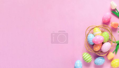 Foto de Feliz Pascua concepto tarjeta de felicitación vacaciones. Huevos de Pascua coloridos y flores de primavera sobre fondo rosa pastel. Vista superior, plano, espacio para copiar. - Imagen libre de derechos