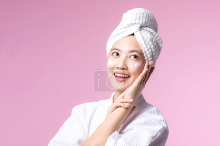 Téléchargez les photos : Asiatique jeune femme appliquant soin du visage crème pour le visage, hydratant cosmétique sur la peau naturelle saine maquillage visage. Portrait lumineux sourire fille personne modèle avec soin produit de beauté, spa, cosmétologie. - en image libre de droit