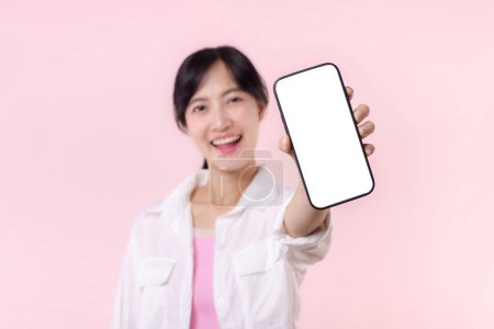 Photo for Happy smiling asian young woman recommending showing new application or mobile advertisement, mockup smartphone template banner isolated on pink background. Collage blank screen digital mobile device. - Royalty Free Image