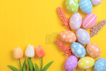 Photo for Happy Easter holiday greeting card concept. Colorful Easter Eggs and spring flowers on yellow background. Top view, flat lay, copy space. - Royalty Free Image