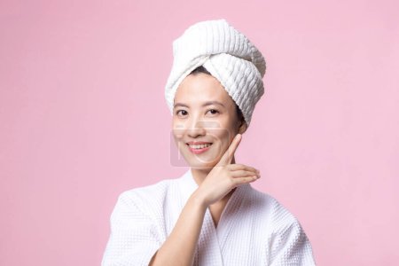 Téléchargez les photos : Jeune belle femme asiatique heureuse avec une peau de visage propre en serviette et peignoir, costume de spa sur fond rose. Soins de la peau, traitement, thérapie de bien-être, soins du visage, beauté santé féminine, concept de cosmétologie - en image libre de droit