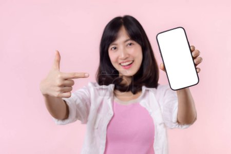 Photo for Happy smiling asian young woman recommending showing new application or mobile advertisement, mockup smartphone template banner isolated on pink background. Collage blank screen digital mobile device. - Royalty Free Image
