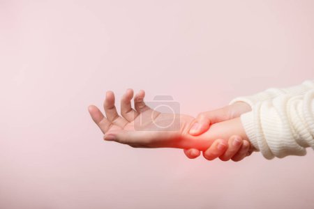 Foto de Mujer joven asiática con suéter blanco que sufre de lesión en la mano de la muñeca dolor. Las causas de dolor incluyen síndrome del túnel carpiano, fracturas, artritis o dedo gatillo. Concepto de salud. - Imagen libre de derechos