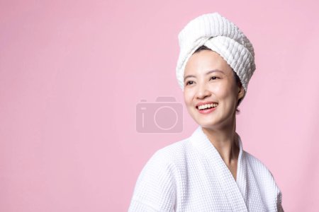 Foto de Joven hermosa mujer asiática feliz con la piel limpia de la cara en toalla y albornoz, traje de spa sobre fondo rosa. Cuidado de la piel, tratamiento, terapia de bienestar, cuidado facial, salud femenina de belleza, concepto de cosmetología - Imagen libre de derechos