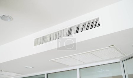 Foto de Acondicionador de aire tipo casete montado en el techo y luz moderna de la lámpara en el techo blanco. acondicionador de aire por conducto para oficina o casa - Imagen libre de derechos