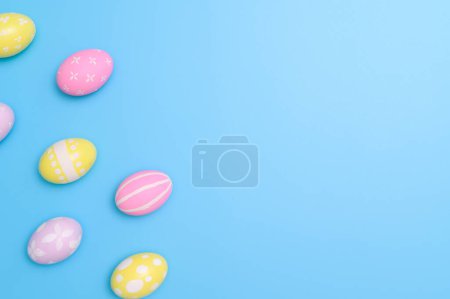 Photo for Happy Easter holiday greeting card concept. Colorful Easter Eggs and spring flowers on blue background. Top view, flat lay, copy space. - Royalty Free Image