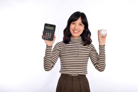 Foto de Retrato de una joven asiática sosteniendo alcancía blanca y calculadora aislada sobre fondo blanco, concepto de ahorro financiero y bancario - Imagen libre de derechos