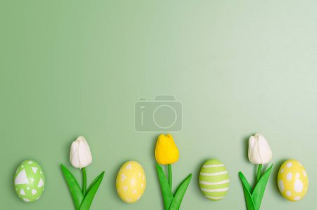 Foto de Feliz Pascua concepto tarjeta de felicitación vacaciones. Huevos de Pascua coloridos y flores de primavera sobre fondo verde pastel. Vista superior, plano, espacio para copiar. - Imagen libre de derechos