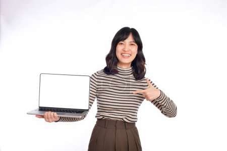 Téléchargez les photos : Jeune femme asiatique sur le tissu pull pointant vers le haut de l'ordinateur portable et regardant la caméra avec le visage sourire et heureux isolé sur fond blanc - en image libre de droit