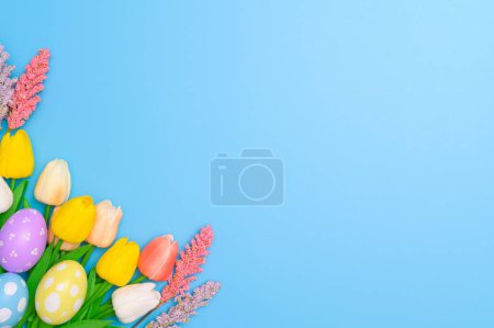 Téléchargez les photos : Bonne fête de Pâques concept de carte de voeux. Oeufs de Pâques colorés et fleurs de printemps sur fond bleu. Vue du dessus, plan, espace de copie. - en image libre de droit