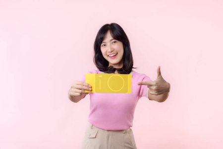 Photo for Portrait young happy woman model holding and showing blank space paper for advertisement information message poster with thumb up or point finger gesture isolated on pink pastel studio background. - Royalty Free Image