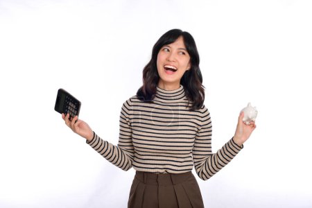 Téléchargez les photos : Portrait of young Asian woman holding white piggy bank and calculator isolated on white background, Financial and bank saving money concept - en image libre de droit