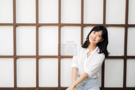 Téléchargez les photos : Portrait beautiful young asian woman happiness sitting on wooden grid wall, Happy female is smiling on wooden grid wall - en image libre de droit